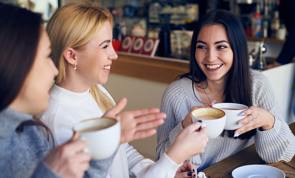 A group of woman smiling and holding cups of coffee while around a table